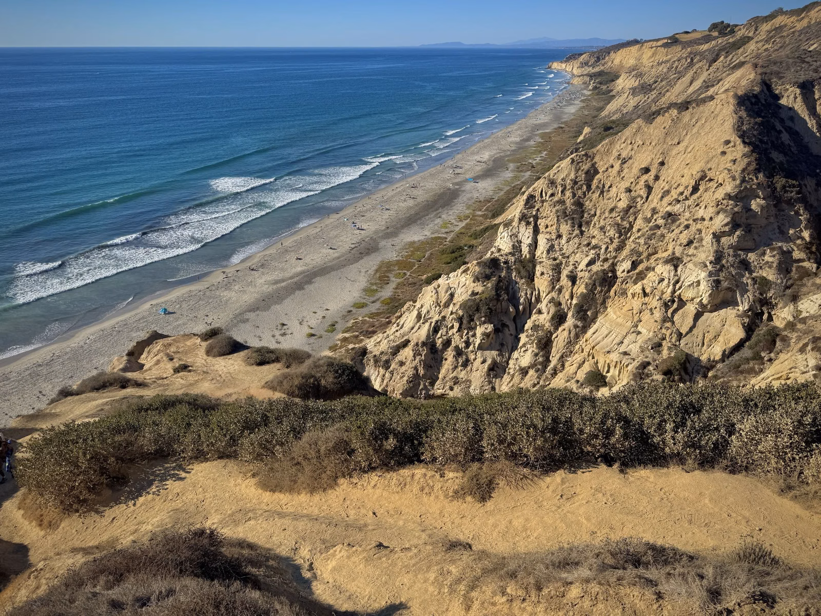 Steep sandstone cliffs above a long sandy beach, seen from the cliff top